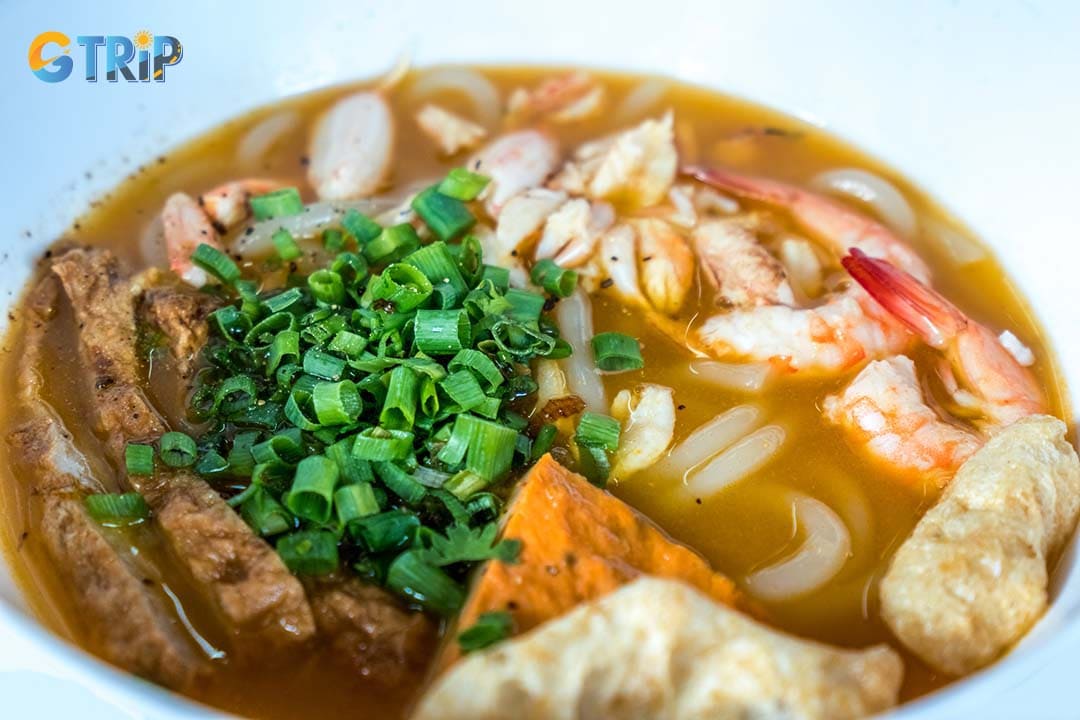Banh Canh Cua is a rich specialty featuring thick, chewy tapioca noodles in a velvety crab-based broth loaded with sweet crab meat, shrimp, fish cakes, and quail eggs