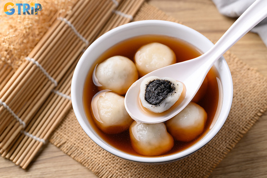 Banh troi Tau is a Hanoi winter favorite, featuring glutinous rice balls with sesame filling in sweet ginger syrup, topped with coconut milk and peanuts