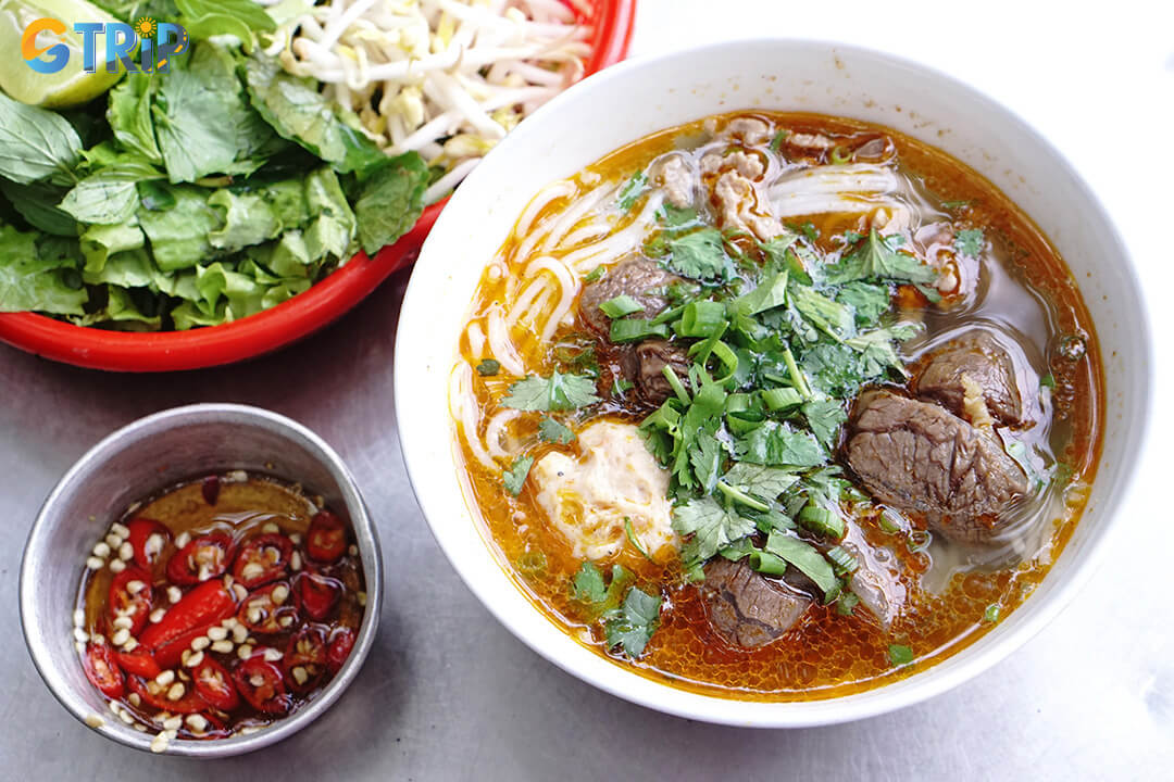 Bun bo Hue is a spicy beef noodle soup with thick vermicelli, tender beef, pork hock, and fresh herbs, offering a hearty, flavorful breakfast in Ho Chi Minh City