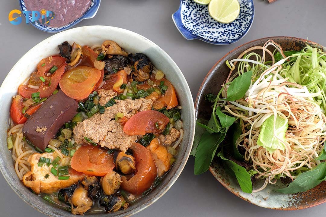 Bun Rieu is a vibrant tomato-based noodle soup topped with soft crab cakes made from fresh crab paste, served with rice vermicelli, tofu, herbs, and pungent shrimp paste