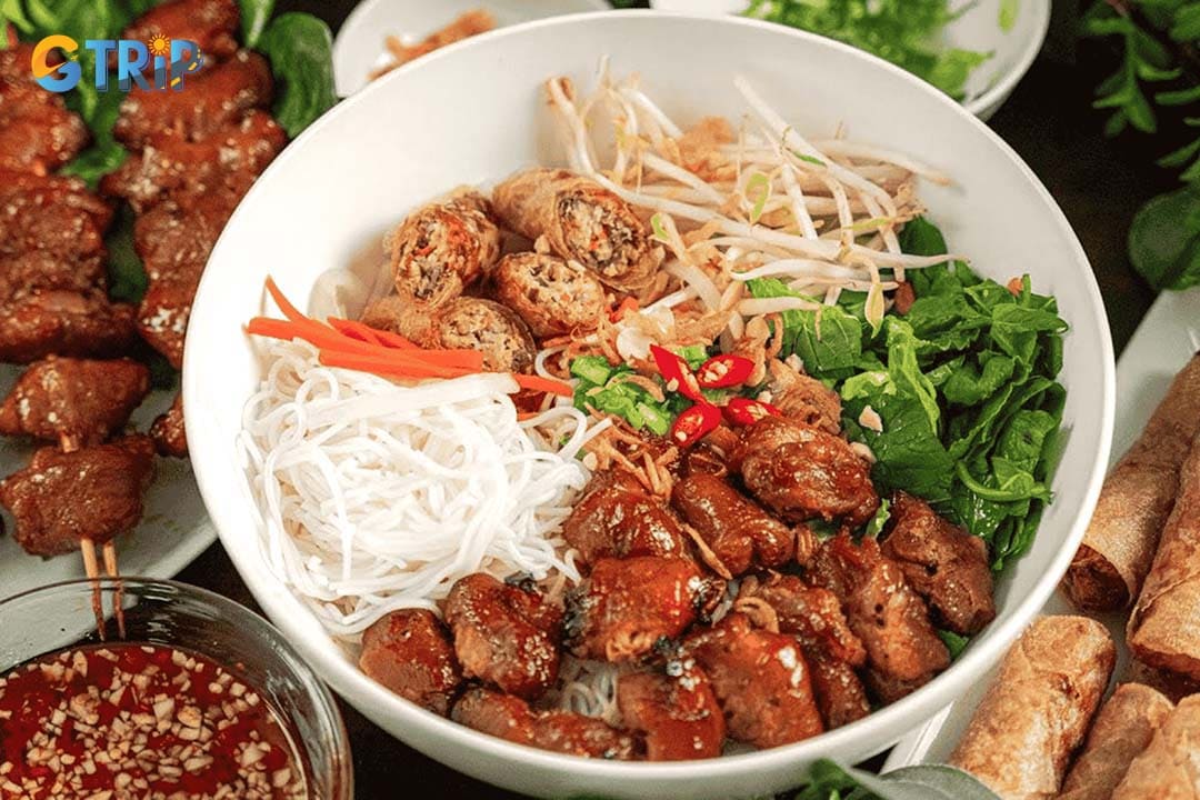 Bun Thit Nuong is a dry noodle dish featuring cool rice vermicelli topped with smoky grilled pork, fresh herbs, pickles, peanuts, and often a crispy spring roll