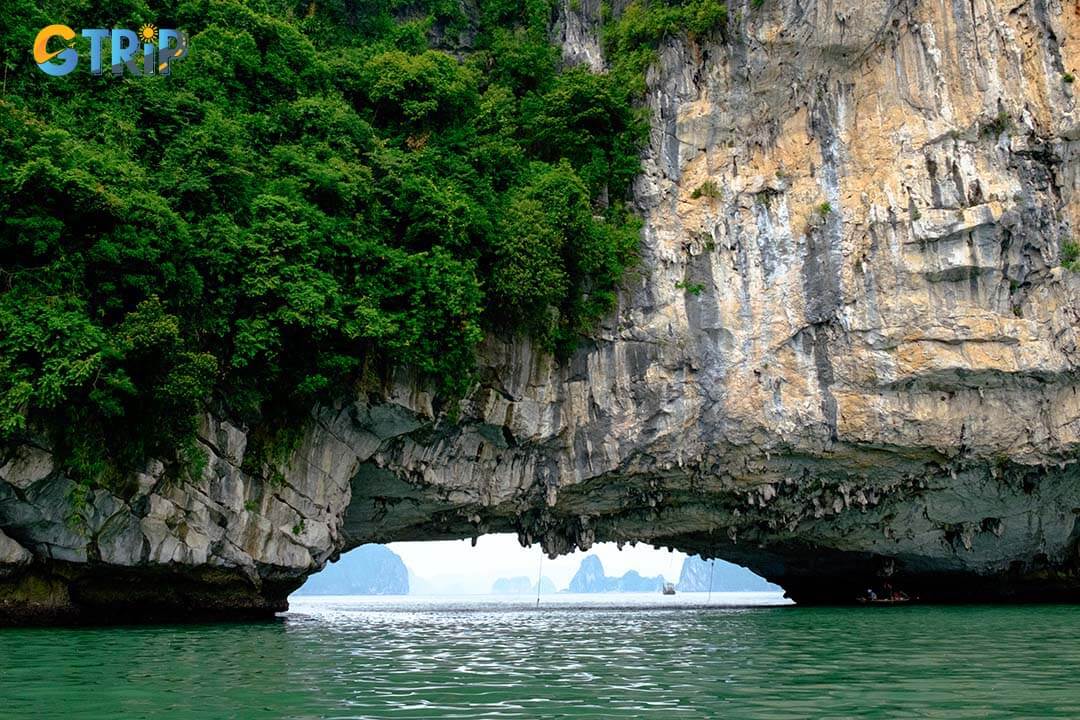 Luon Cave offers a unique adventure, where kayakers navigate through a towering archway into a tranquil, cliff-surrounded lagoon