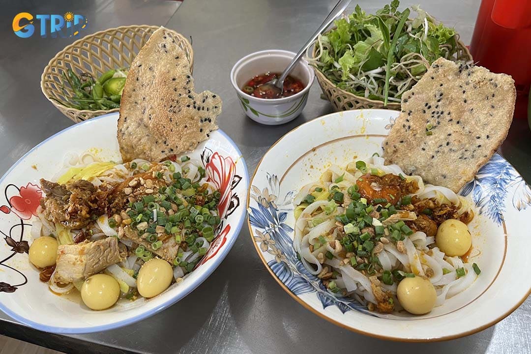 Mi Quang Phu Chiem is known for its lively morning atmosphere, budget-friendly prices, and richly seasoned turmeric noodles topped with fresh, traditional ingredients