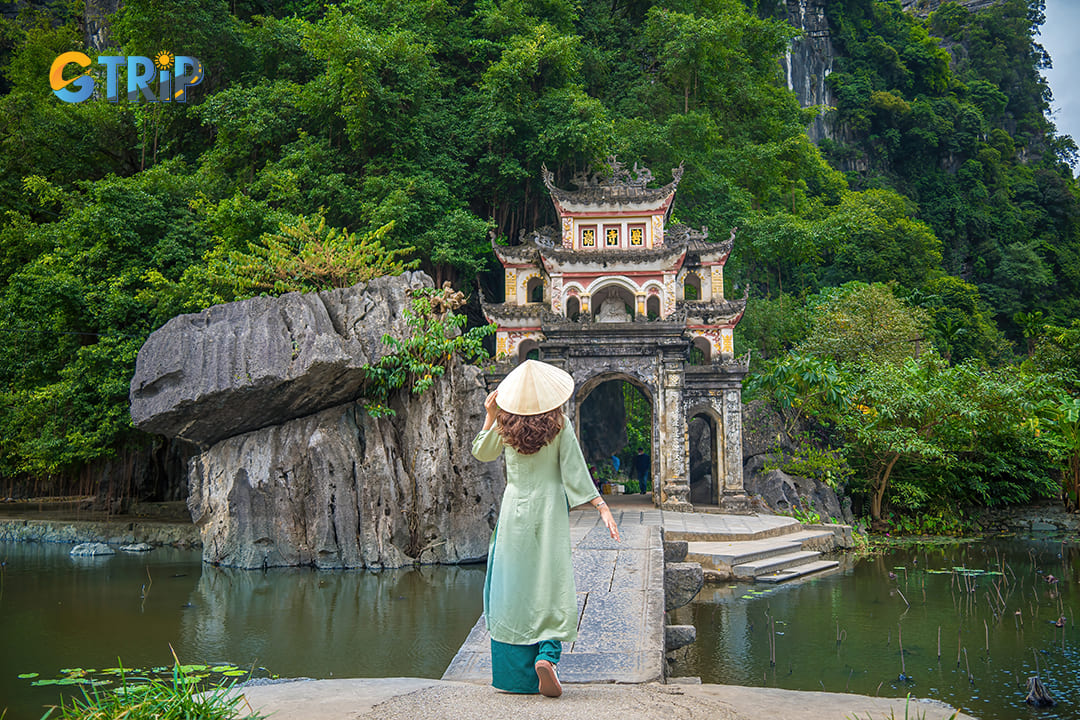 Girl wearing ao dai walks across the stone bridge leading into the Bich Dong Pagoda