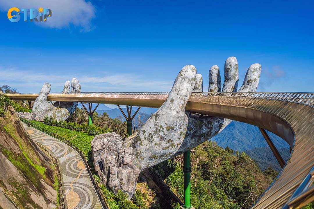 The 150-meter-long Golden Bridge curves gracefully above a lush valley, featuring a wooden walkway, golden railings, and iconic giant hands crafted from steel