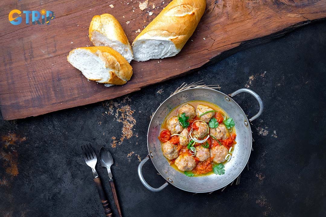 The Banh Mi xiu mai chen features tender pork meatballs simmered in a light tomato sauce, served with a generous spoonful of savory