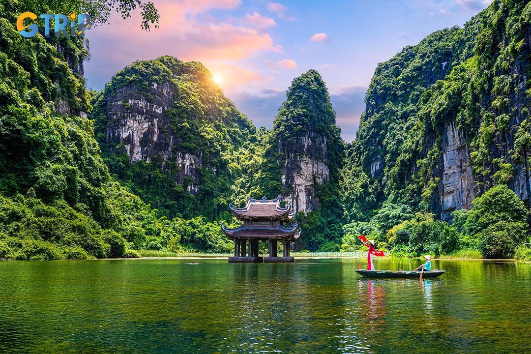 Asian women wearing red traditional Vietnamese cultural clothing on a boat floating in the river flowing through the mountains at Trang An